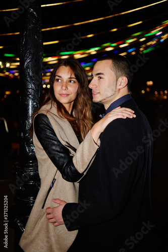 Portrait of beautiful young lovers standing in the night city with beautiful lights on background