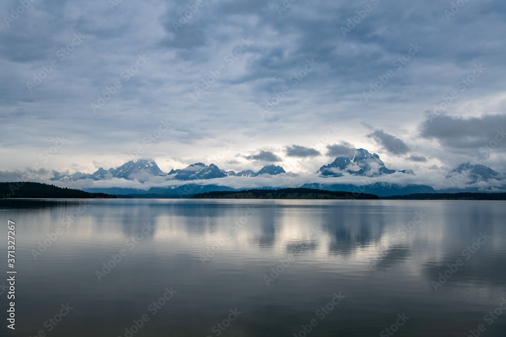 A cloudy day at Jackson Lake in Wyoming, USA at the Grand Teton National Park. Low lying clouds are surrounding the mountains and reflecting onto the lake. 