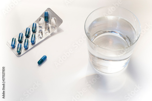 blister pack of blue pills and a glass of water over a white bacground