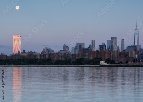 View on Downtown Manhattan from East river at sunrise with full moon set .