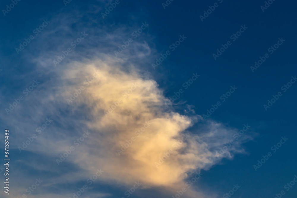 thin white cloud, blown by the winds, shaded by yellow, floating under a blue sky.