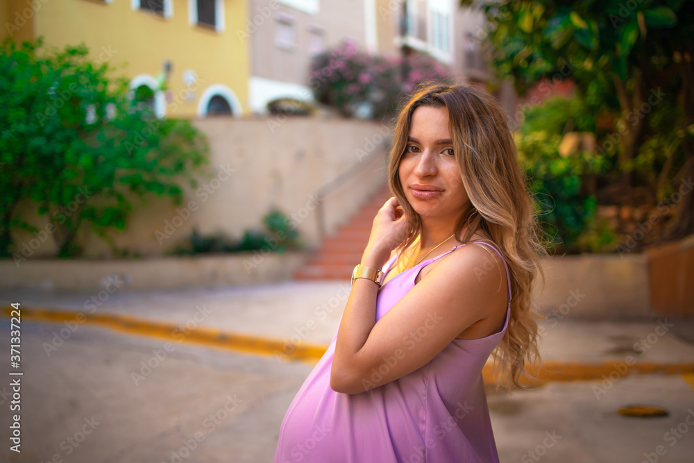 beautiful pregnant woman in a purple dress stands in the old city, hold she hands on belly . Looking into the camera, close up 