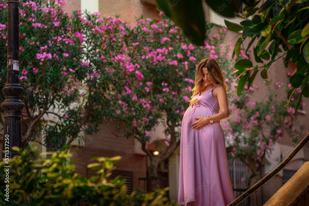 beautiful young pregnant girl in a purple dress stands on the stairs against the background of a flowering tree