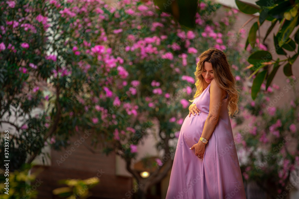 Fototapeta premium beautiful young pregnant girl in a purple dress stands on the stairs against the background of a flowering tree