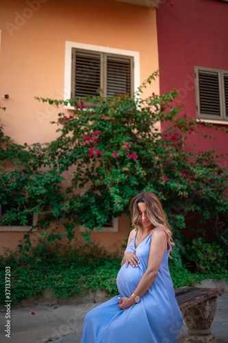 beautiful pregnant girl holding her belly and sitting on a bench overlooking the garden in old city 