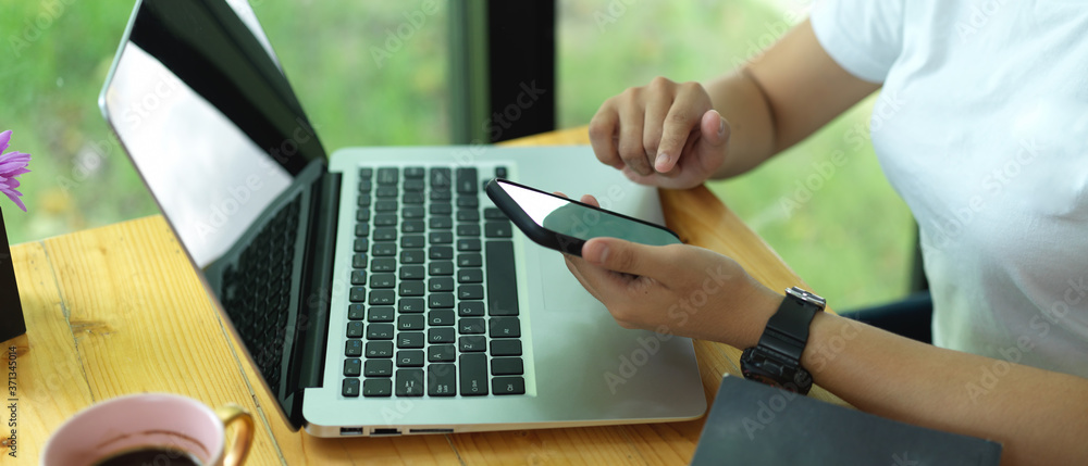Female college student using mock up smartphone while doing homework with laptop