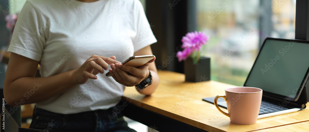 Obraz premium Female using smartphone while sitting at worktable with mock up tablet