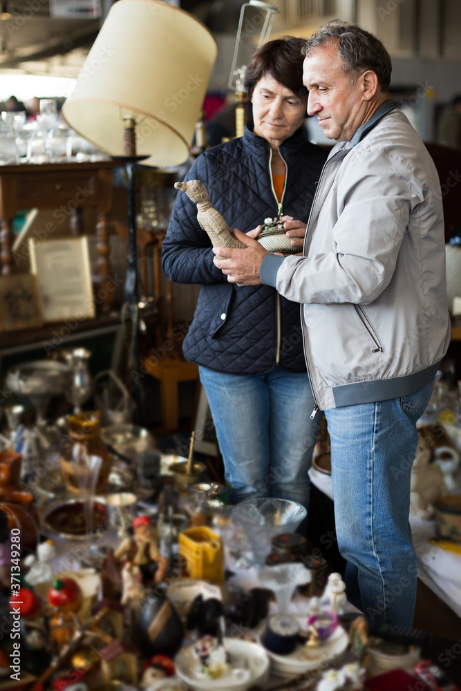 Senior man and female choosing interesting souvenirs at traditional flea market
