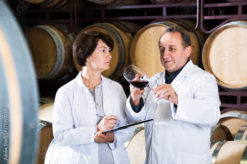 Smiling wine maker examining quality of wine by means of wineglass in bodega photo