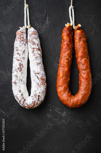 Spanish salami, fuet and chorizo sausages hang from a rack on black background