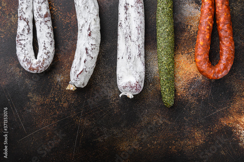 Dry cured chorizo and fuet salami sausages hanging on dark background with copy space