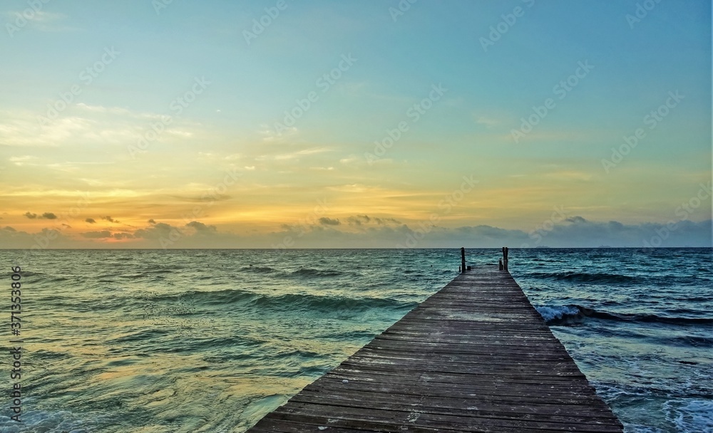 Early morning in the Caribbean. Dawn begins. The sky is painted in golden hues. Waves on the sea. There is a wooden path over the water. Mexico.