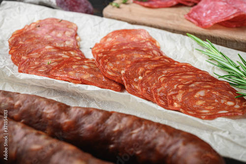 Variety of dry cured chorizo, fuet and other sausages cut in slices with herbs on old wooden table