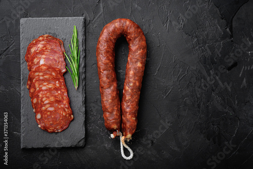 Whole and sliced chorizo sausage on black background, flat lay with copy space