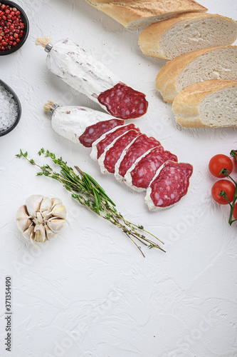 Spanish salcichon slices with panini and herbs on white textured background, topview with space for text