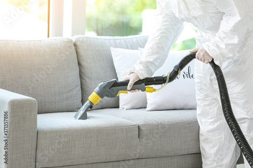 Worker in biohazard costume removing dirt from sofa in house photo