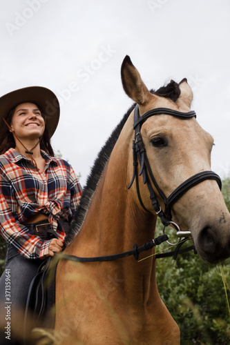 Young cow girl walking horse in green field. People and animal portrait. Horseback riding view. Active weekend