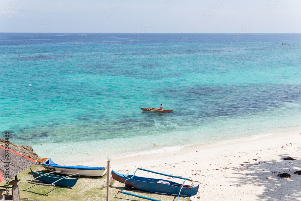 Unrecognizable Filipino man on small catamaran on paradise beach with turquoise water and white sand in Philippines