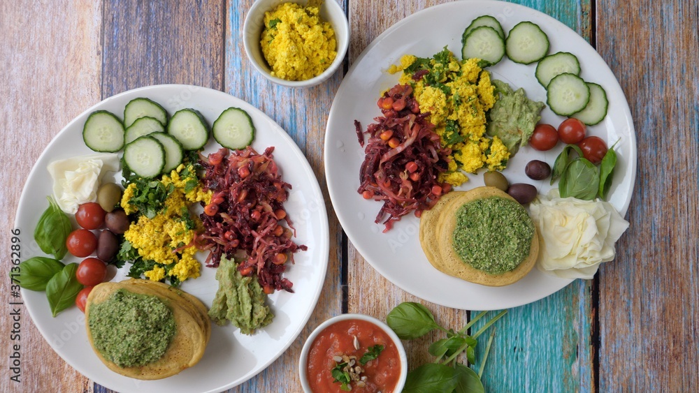 Top view of healthy organic vegan breakfast featuring tofu scramble, pancakes, dips and vegetables. Wooden table background. Healthy lifestyle concept.