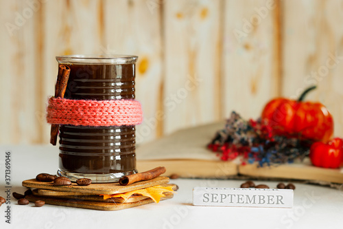 black coffee glass mug in cute scarf coffee beans, cinnamon, wild flowers, book, pumpkins and autumn leaves and inscription September. Autumn cozy coffee image