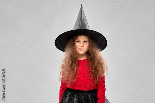halloween, holiday and childhood concept - girl in costume and witch hat over grey background