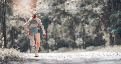 Rear view of young sportswoman start running outdoors in the park with sunlight in the morning.