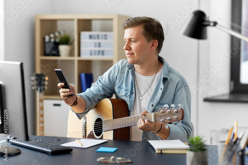 leisure, music and people concept - young man or musician with guitar and smartphone sitting at table at home