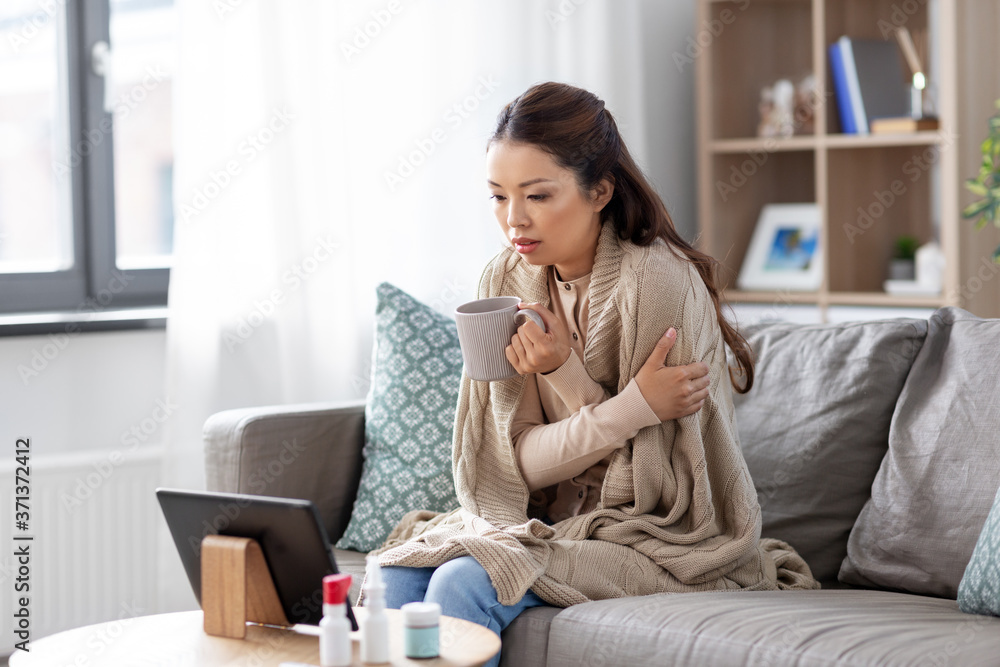 medicine, healthcare and technology concept - sick young asian woman having video call or online consultation on tablet pc computer and drinking tea at home medicine, healthcare and technology concept - sick young asian woman having video call or online consultation on tablet pc computer and drinking tea at home