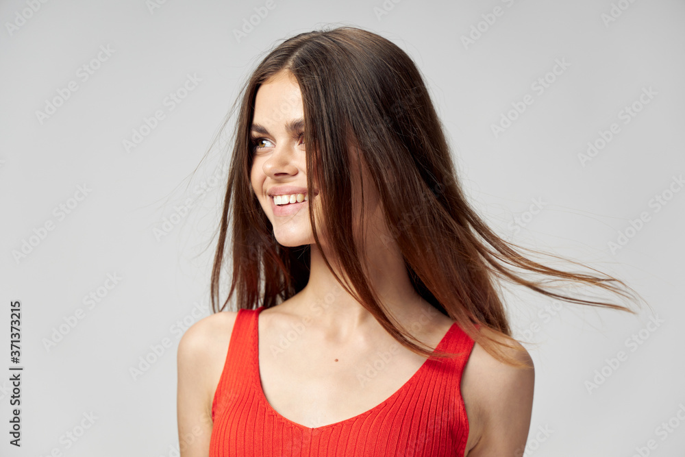 A joyful brunette woman in a red T-shirt turned her head to the side on a light background A joyful brunette woman in a red T-shirt turned her head to the side on a light background
