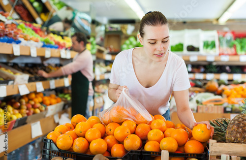 Young woman customer choosing fresh oranges on the supermarket