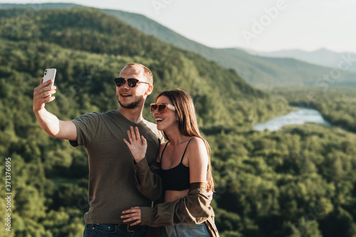 Young Traveler Couple on a Trip, Man and Woman Using Smartphone for Video Call, Bloggers Making Selfie Over Beautiful Landscape