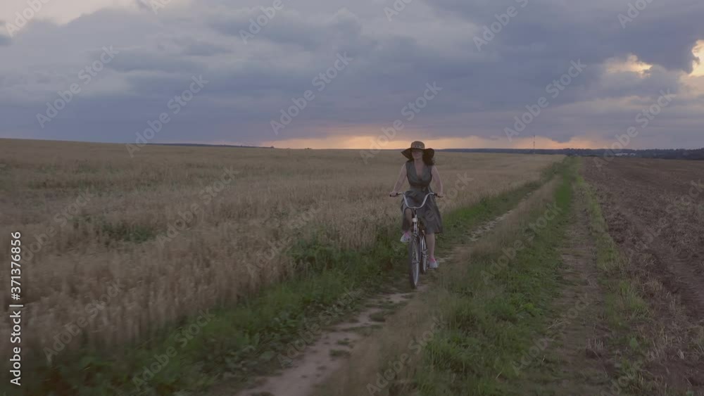 beautiful woman enjoys walking bike ride while riding path in wheat field at sunset. beautiful woman enjoys walking bike ride while riding path in wheat field at sunset.