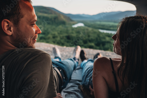 Rear View of Happy Young Couple Lying in the Trunk of Their Car and Enjoying Roadtrip, Mountains and River on the Horizon