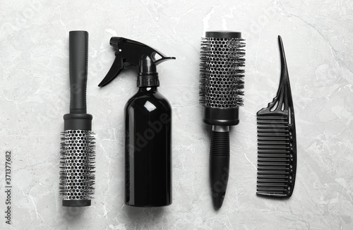 Hair brushes, comb and spray on light grey marble background, flat lay