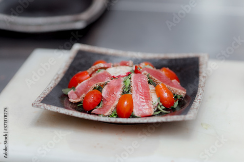 beautiful top view of a ready-made healthy dish on a white board in a restaurant fish pieces sprinkled with sesame seeds, tomatoes and herbs