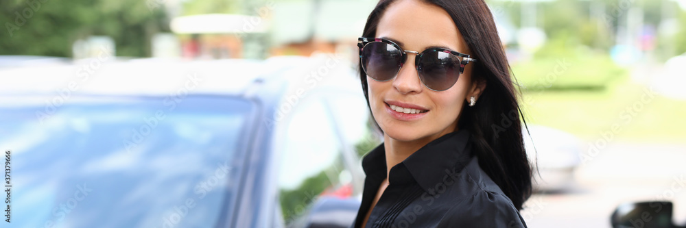 Beautiful woman in sunglasses stands near a car