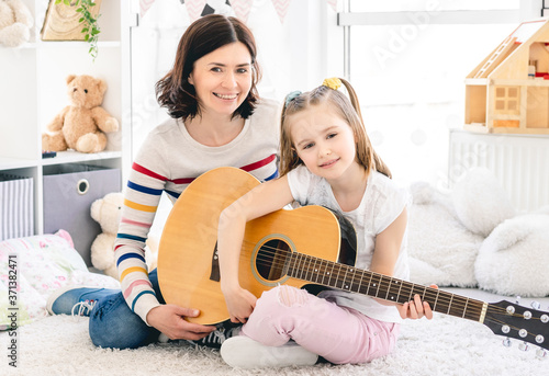 Happy mother with cute daughter playing guitar at home