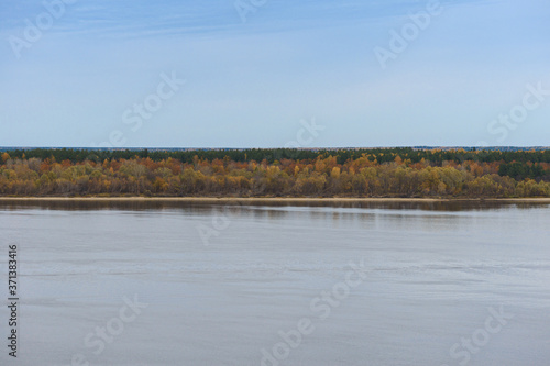 Distant sandy riverbank with autumn forest on a cloudy afternoon