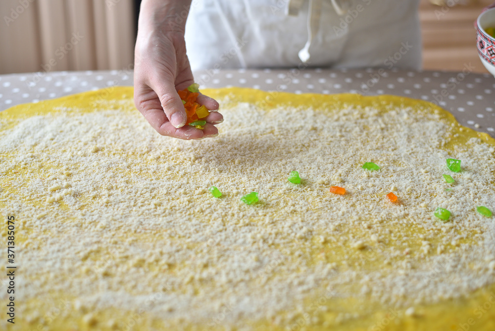 woman's hand sprinkles the dough with candied fruits and raisins woman's hand sprinkles the dough with candied fruits and raisins