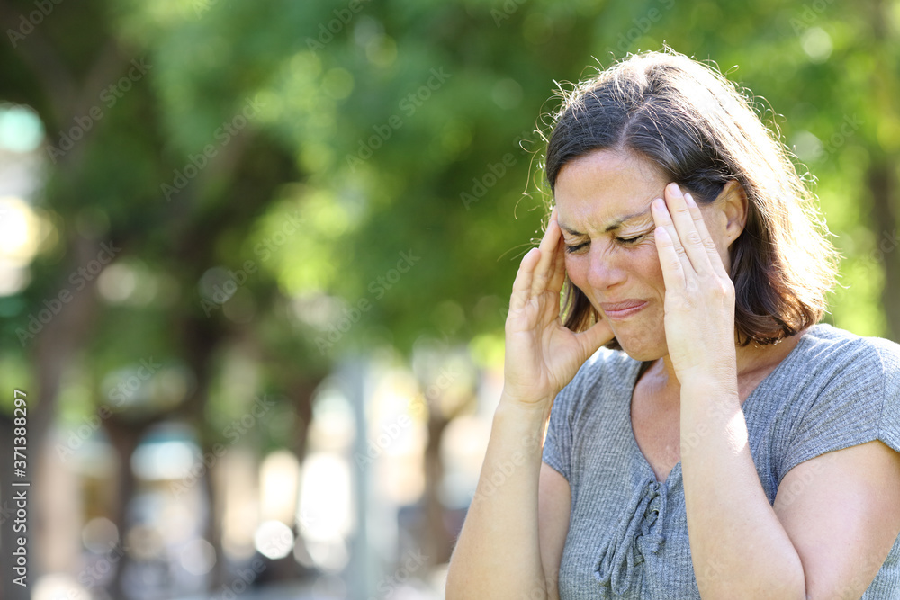 Adult woman suffering a migraine standing in the park