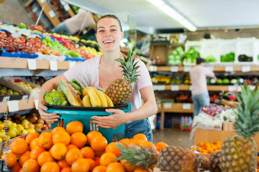 Cheerful woman standing with full shopping cart during shopping in fruit store