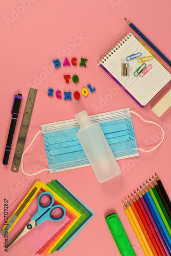 School stationery, protective mask, alcohol gel, on pink background. Back to school after covid-19 coronavirus. Learning concept.
