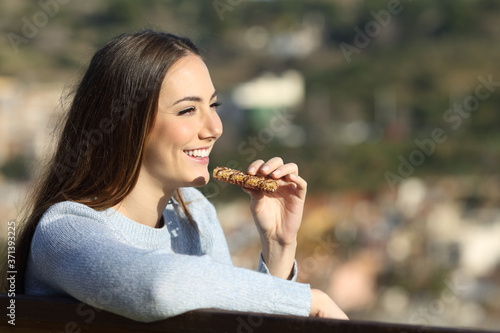 Happy woman eating cereal bar on a park bench