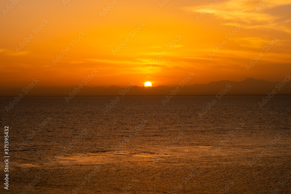 Minimal orange sunset over the Red Sea and Sudanese mountains on the horizon, tranquil evening, seen from a ship.