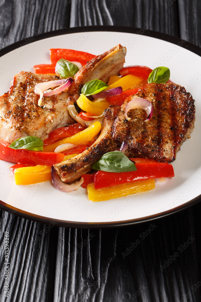 Grilled spicy pork chop with stewed yellow and red bell peppers and onions close-up in a plate on the table. vertical Grilled spicy pork chop with stewed yellow and red bell peppers and onions close-up in a plate on the table. vertical