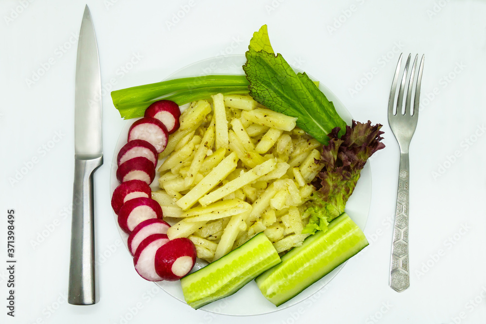 Fried potatoes with spices, chopped radish, cucumbers, green onions, lettuce. Knife and fork lying nearby Fried potatoes with spices, chopped radish, cucumbers, green onions, lettuce. Knife and fork lying nearby