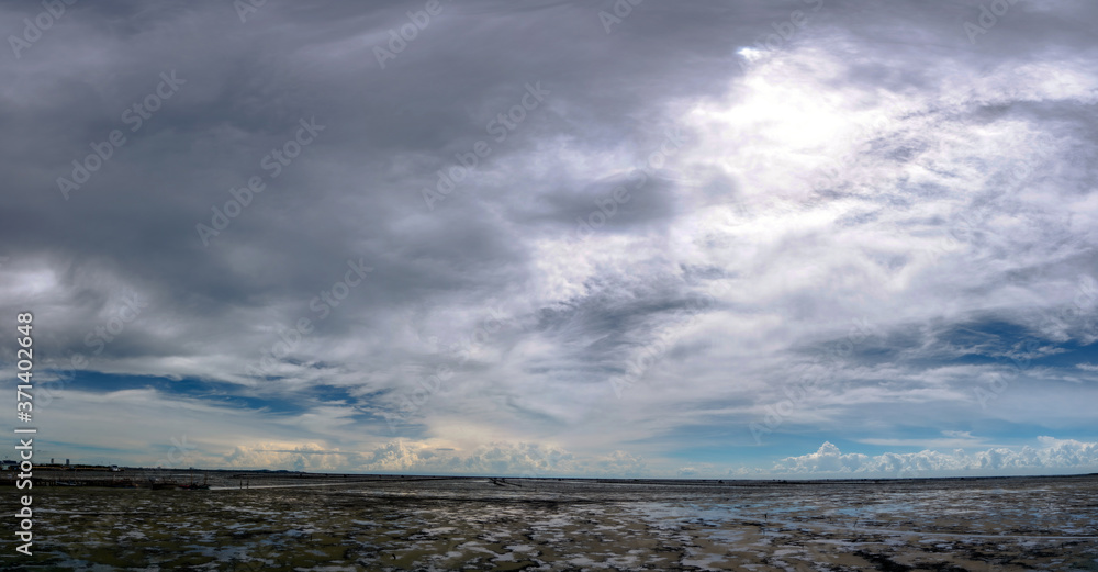 Landscape of mud beach, sea, and sky. Panorama view of beach at tide and skyline. Beautiful cloudscape. Blue sky and white clouds on sunny day. Tropical sea. Summer travel concept. Climate change.