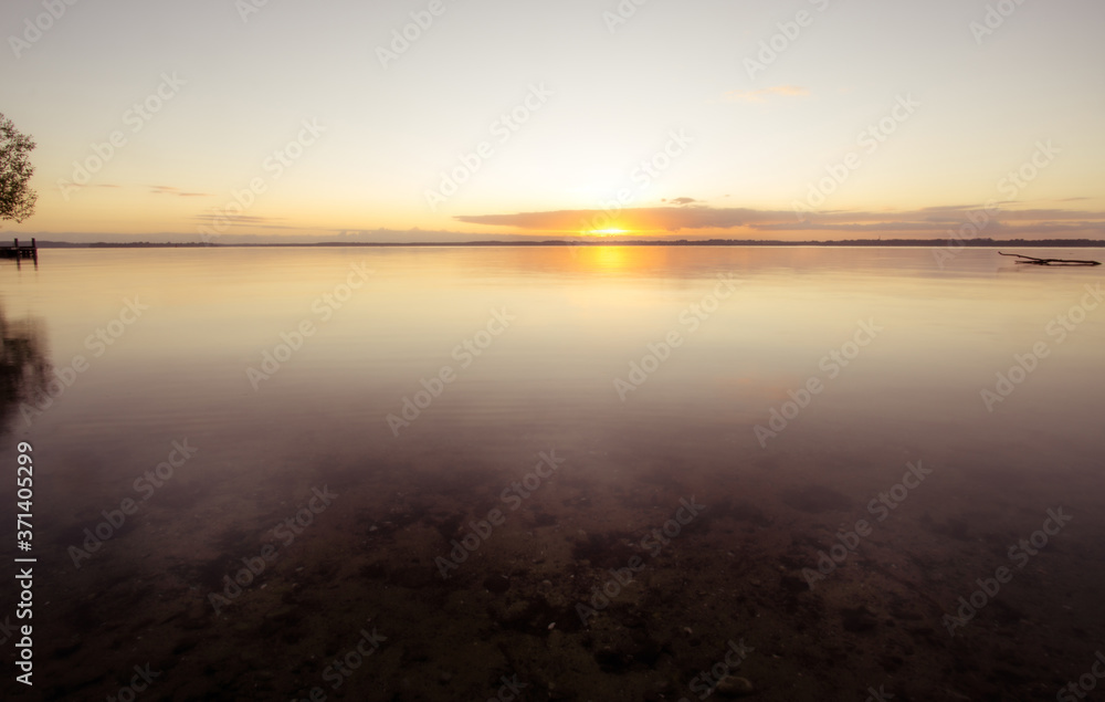 Sonnenaufgang am See bei ruhigen Gewässer mit Treibholz