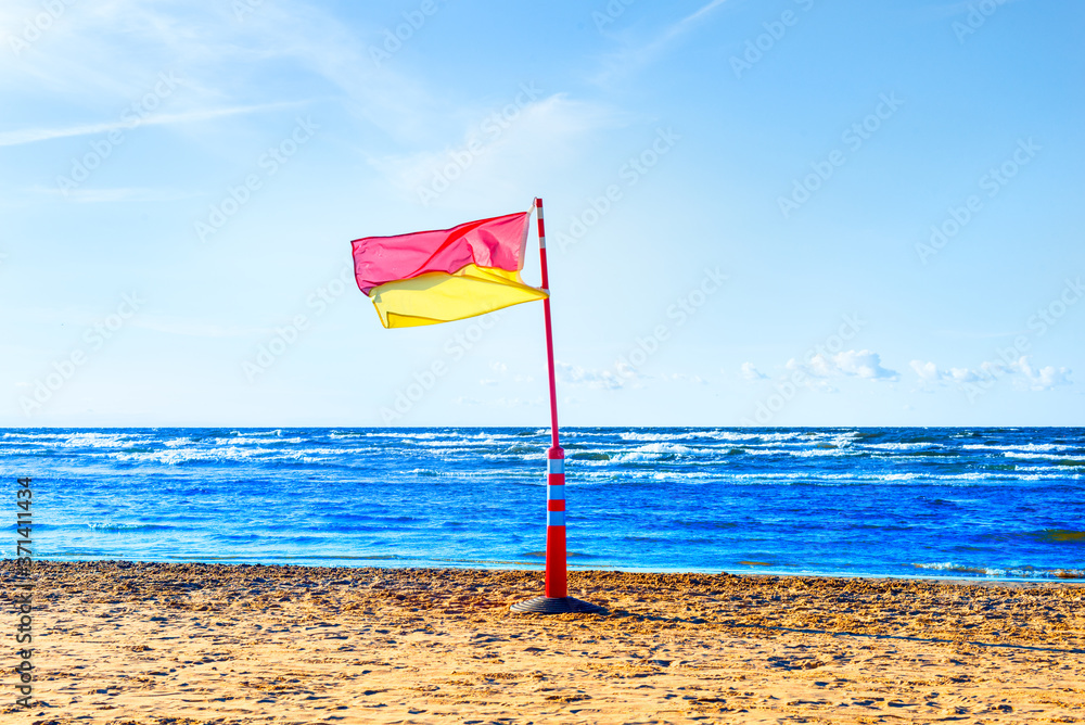 Red, yellow life saving flag on the sea beach on blue sky