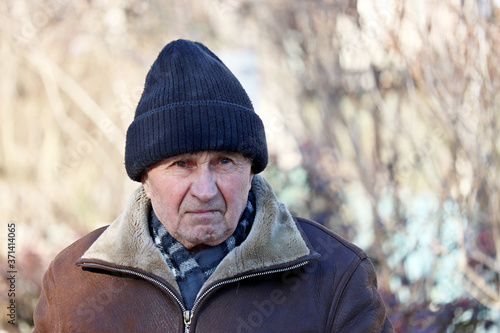 Portrait of unhappy elderly man standing outdoor. Concept of cold weather, life in village, old age © Oleg